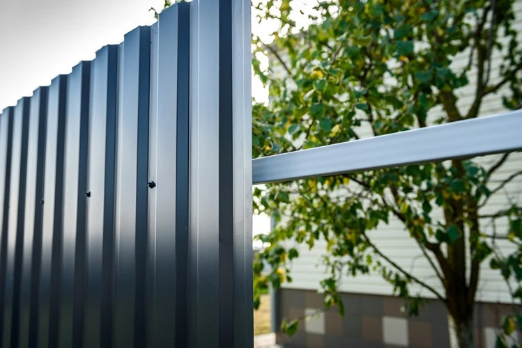 Fence-Installation-installation-gray-fence-metal-profile Close-up of a modern grey metal fence panel with garden and house in background.