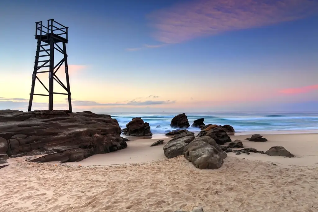 Lake-Macquarie-Redhead Wooden lookout tower on rocky outcrop overlooking redhed's sandy beach and ocean at sunset.