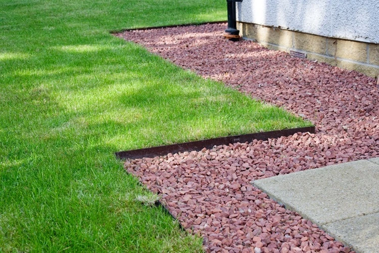 garden-borders-lawn-edging-made-metal-showing-straight-500px Clean metal edging separating green lawn from reddish gravel mulch beside a house