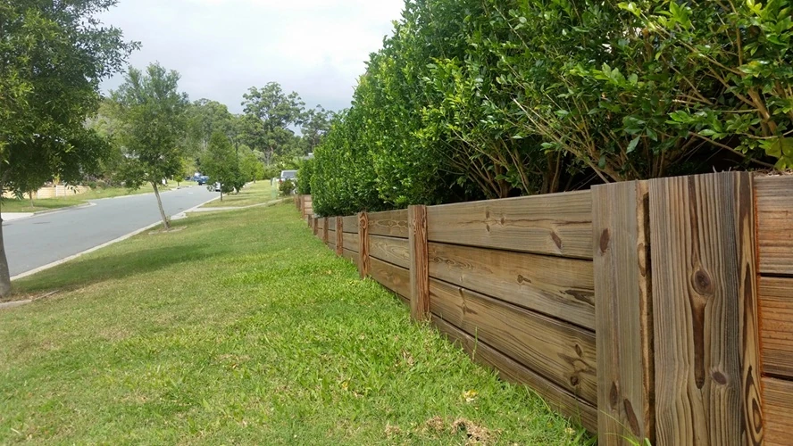 timber-retaining-wall-front-yard-500px Wooden retaining wall supporting garden hedge along suburban street lawn.